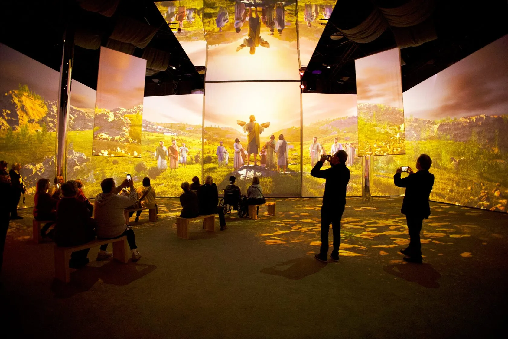 A large projection gallery with visitors seated in front of surrounding screens.