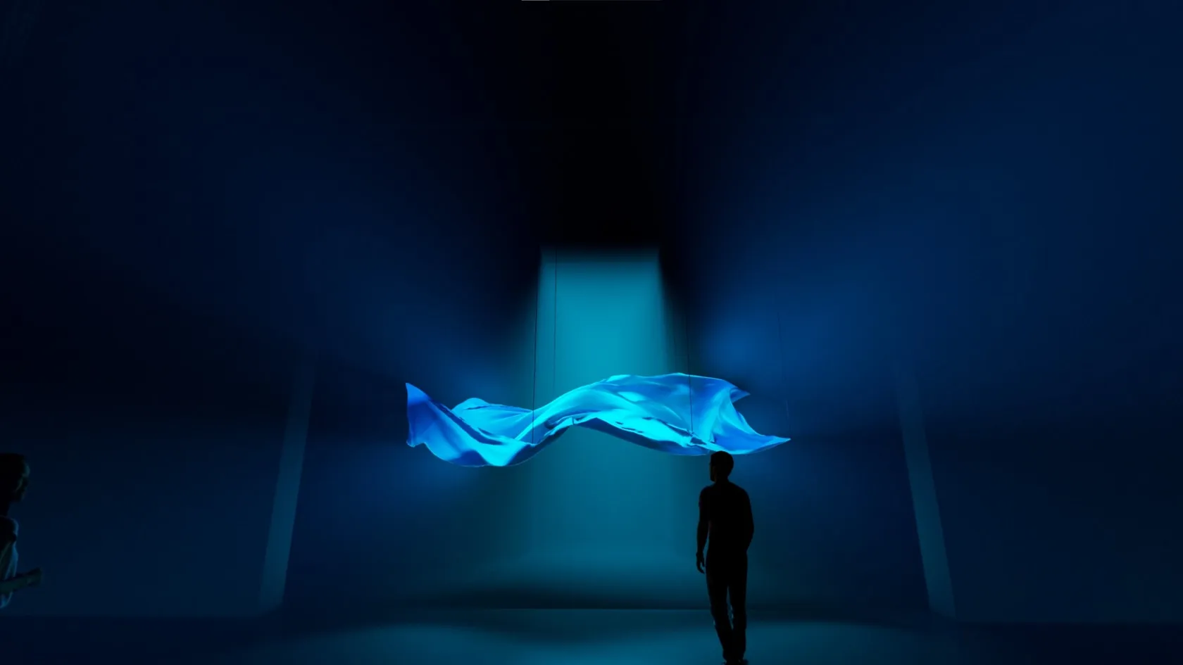 A suspended, illuminated fabric installation in a darkened blue room.
